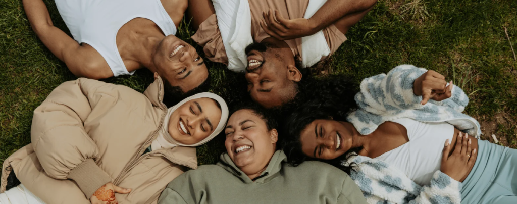 An image of a group of diverse students from different cultures and ethnicities laying on the ground in a circle.
